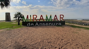 Cartel con el texto Miramar de Ansenuza sobre un suelo de arena, con palmeras, una torre y el agua al fondo.