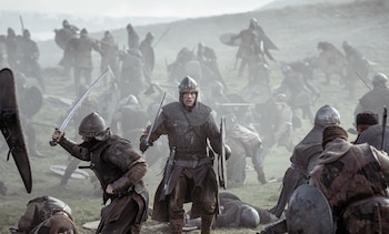 Nikolaj Coster-Waldau, con armadura y casco, empuña una espada y un escudo en un campo de batalla lleno de guerreros armados y caídos bajo un cielo nublado