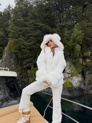 Poggio, en la proa de la lancha, con campera blanca con capucha de piel y Moon Boots a tono