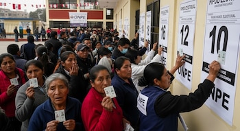 Vista de votantes peruanos haciendo cola en un colegio para las elecciones. Sostienen sus DNI y buscan información en carteles con números de mesa.