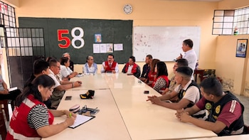 Un grupo de personas se reúne alrededor de una mesa larga en un salón de clases con una pizarra verde al fondo