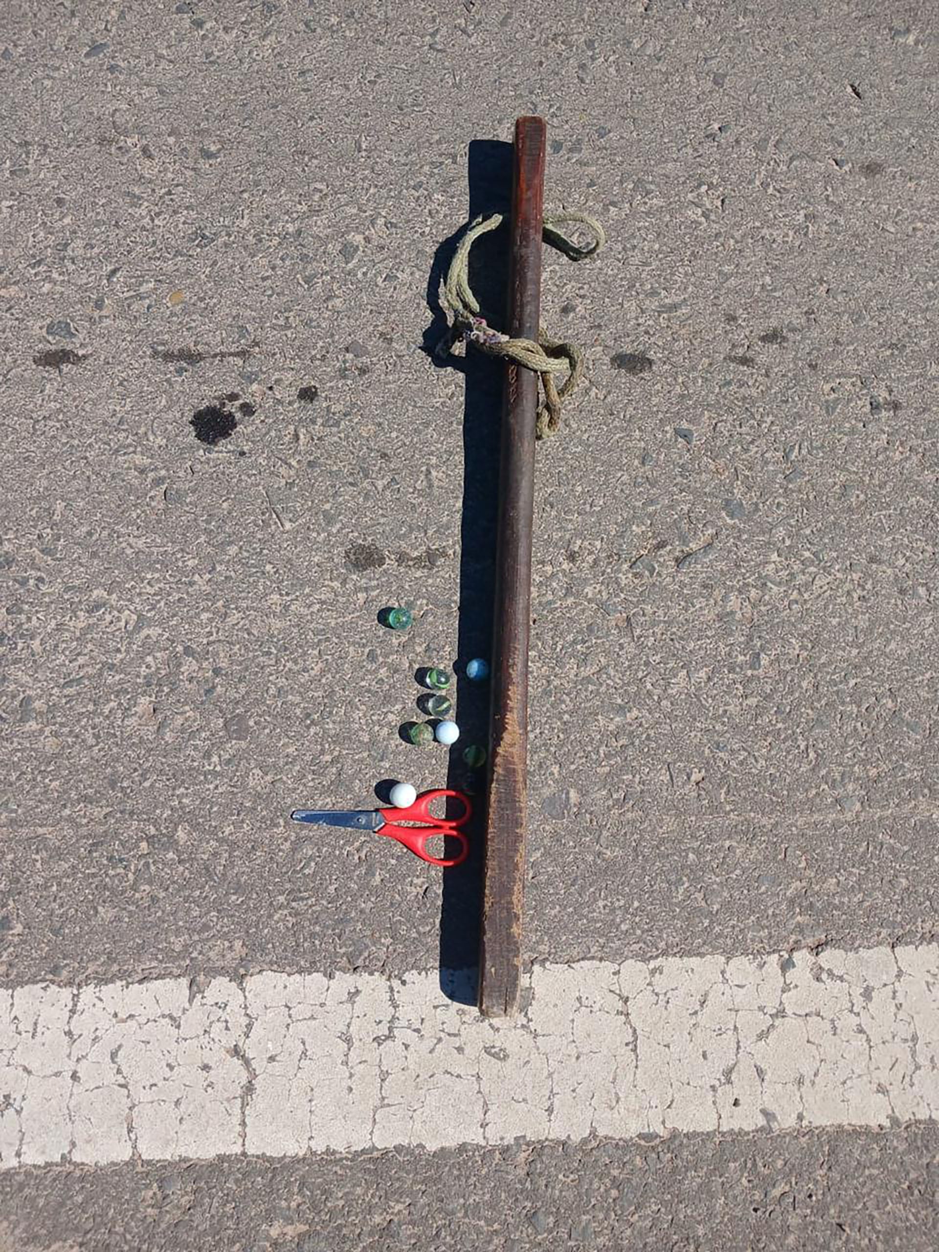 Objetos como una vara de madera, canicas de colores y unas tijeras con mango rojo yacen sobre el asfalto, parte de los elementos hallados tras un intento de corte de ruta impedido por la policía en Chaco.