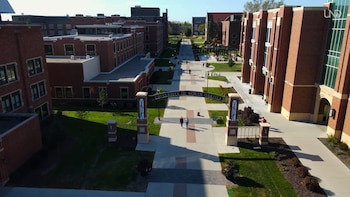 Vista aérea de un campus universitario con edificios de ladrillo rojo, senderos, césped verde y arbustos. Un arco sobre un sendero dice Universidad de Dakota del Norte