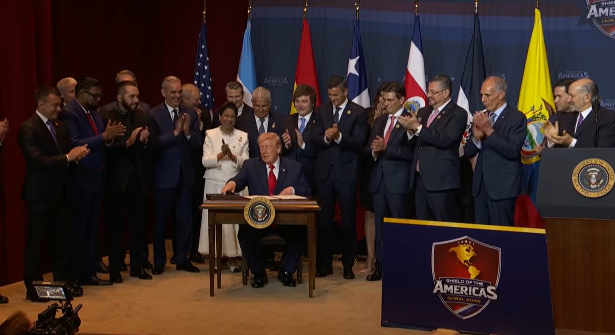 Altos funcionarios de varias naciones se congregan en una convención oficial, con banderas nacionales de fondo y un podio con el sello presidencial, para discutir importantes asuntos. (Cumbre Escudo de las Américas)