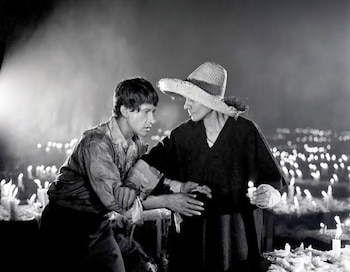 Fotografía en blanco y negro de un hombre y una mujer con sombrero de paja en un espacio oscuro iluminado por numerosas velas encendidas
