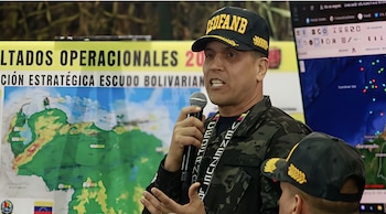 Un hombre con uniforme militar y gorra negra con el logo "CEFANB" habla en un micrófono, con un mapa de Sudamérica y una pantalla digital al fondo