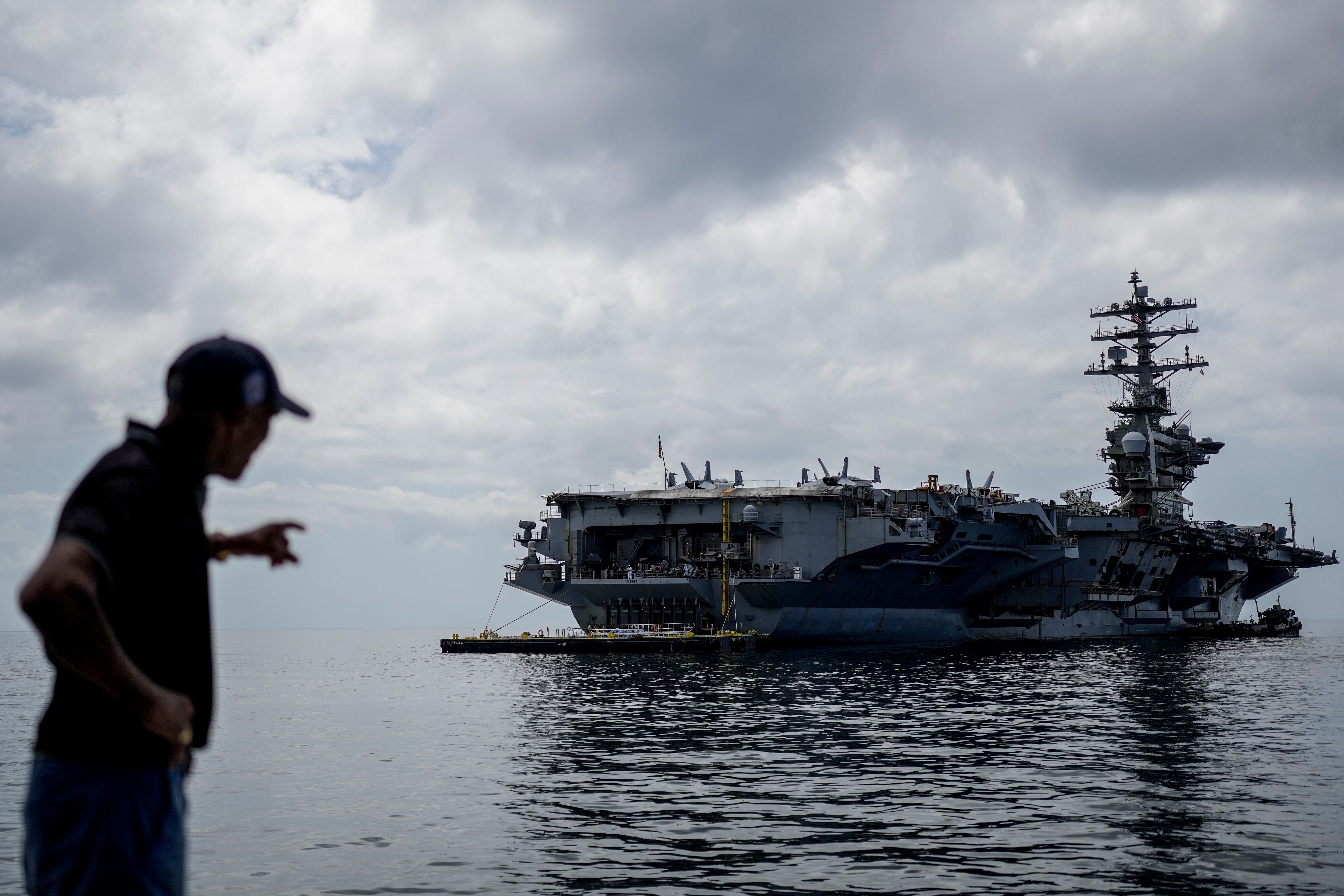 Un trabajador señala el portaaviones de la Armada estadounidense USS Nimitz atracando en el Golfo de Panamá, el lunes 30 de marzo de 2026 (Foto AP/Matias Delacroix)