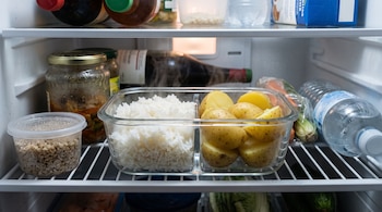 Recipiente de vidrio dividido con arroz blanco y papas en el estante de un refrigerador abierto junto a otros envases y alimentos.