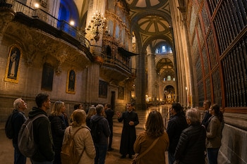 Un sacerdote con sotana habla frente a un grupo de personas en el interior de una catedral iluminada junto a un gran órgano de tubos.