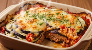 Primer plano de un pastel de berenjena, atún y tomate gratinado en una fuente de cerámica rectangular, humeando, con una porción ya servida.