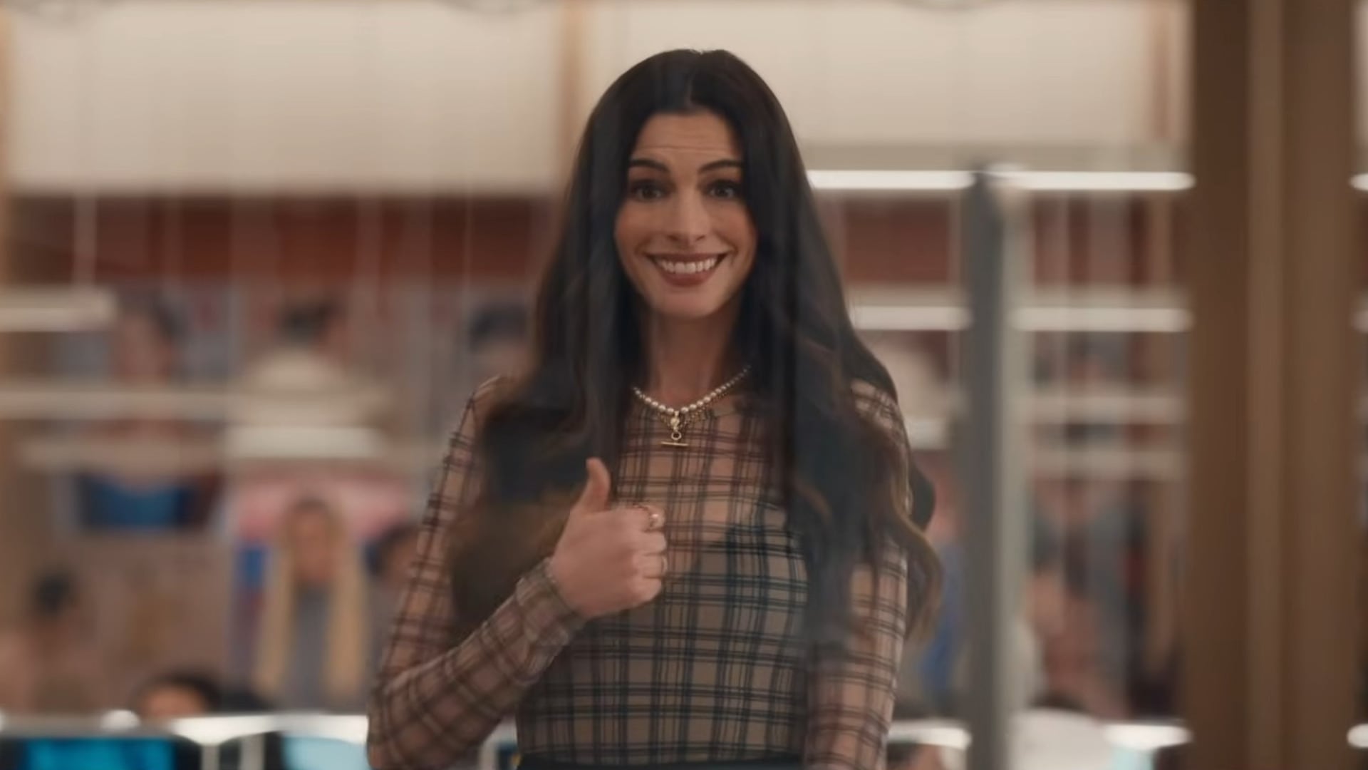 La blusa translúcida de cuadros tierra y accesorios dorados evocan optimismo y ligereza en una oficina iluminada (Captura de tráiler oficial)