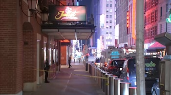 Escena del crimen nocturna en Times Square con un edificio de ladrillo, cinta policial amarilla y un vehículo de la policía de Nueva York