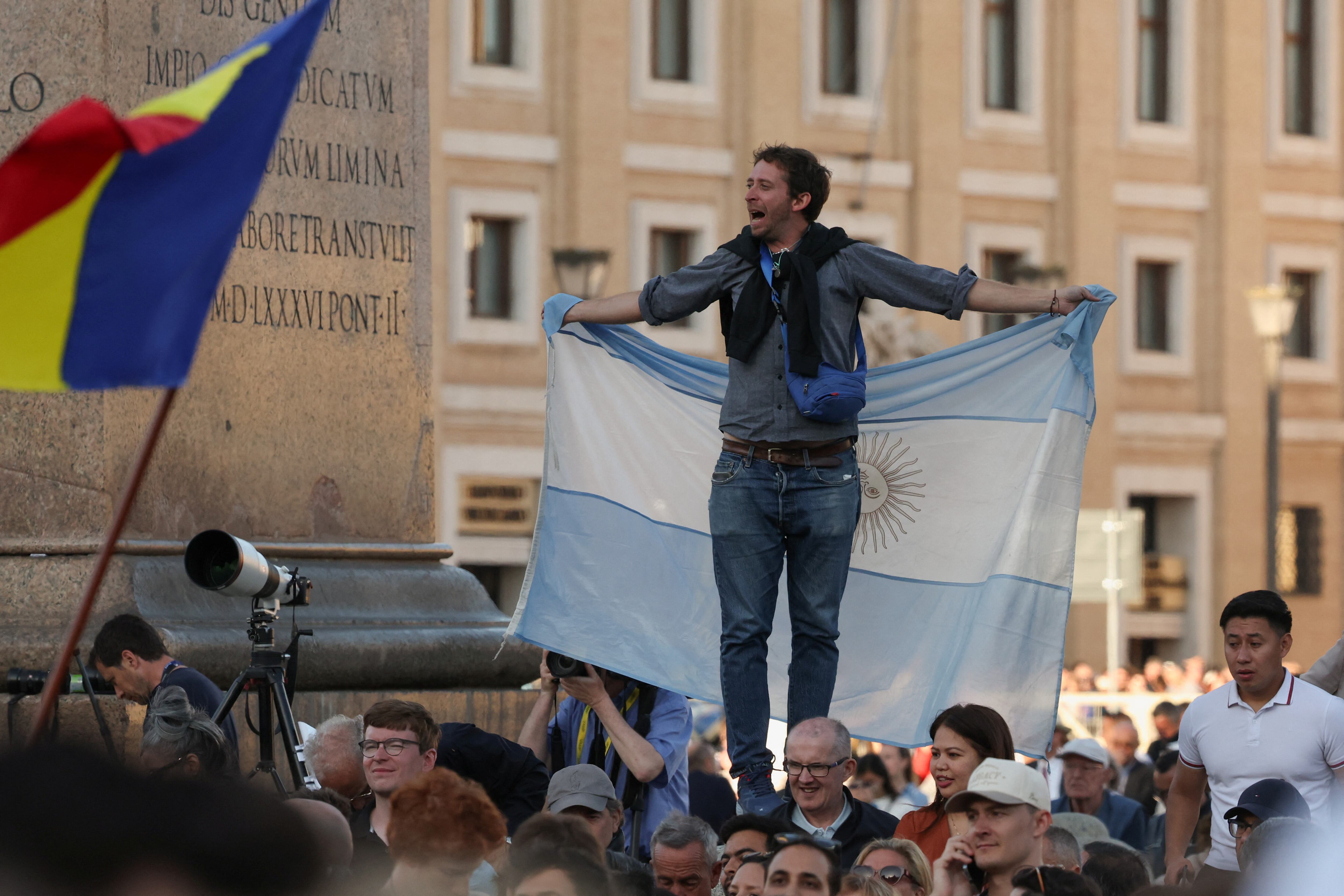 Una persona sostiene una bandera argentina mientras los fieles reaccionan al humo blanco que sale de la chimenea de la Capilla Sixtina, lo que indica que se ha elegido un nuevo papa, en el Vaticano, el 8 de mayo de 2025