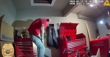 Un hombre con camiseta roja y vaqueros es visible desde la perspectiva de una cámara corporal en un garaje, rodeado de cajas y herramientas rojas