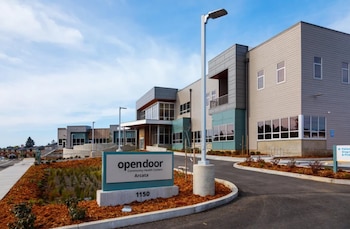 Edificio moderno de Open Door Community Health Centers Arcata con fachada gris, grandes ventanas, entrada de vehículos y paisajismo con mantillo marrón