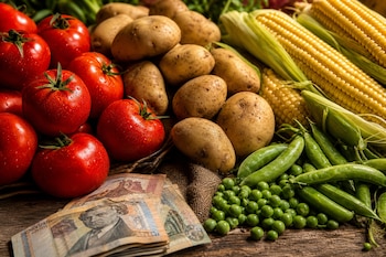 Tomates rojos, papas, mazorcas de maíz, arvejas y un fajo de billetes de soles sobre una mesa de madera.