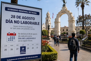 Un panel informativo sobre un día no laborable se ubica en un paseo peatonal frente a un arco monumental de piedra y jardines