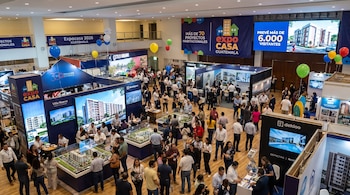 Gran salón concurrido por personas, múltiples stands de exhibición, pantallas con edificios, maquetas arquitectónicas, pancartas de Expocasa 2026, globos.