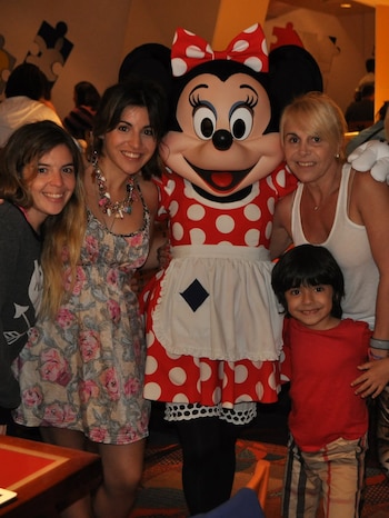 Claudia Villafañe, Gianinna Maradona y un niño sonríen y posan abrazados con el personaje de Minnie Mouse en un interior con poca luz