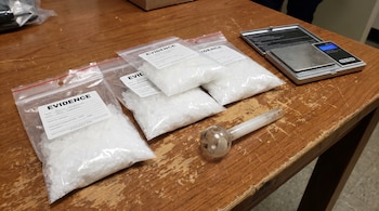 Cuatro bolsas plásticas transparentes con metanfetamina, una pipa de vidrio usada y una balanza digital metálica sobre una mesa de madera marrón.