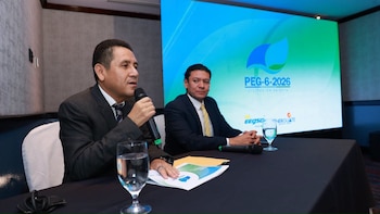Dos hombres en traje sentados ante una mesa con micrófonos y una pantalla azul que muestra el logotipo de la licitación PEG-6-2026