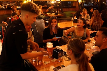 Un camarero atiende a varias personas sentadas alrededor de una mesa de madera con vasos de cerveza en un restaurante