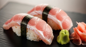 Primer plano de dos piezas de sushi nigiri de otoro sobre una tabla oscura. A la derecha, wasabi verde y jengibre encurtido rosado.