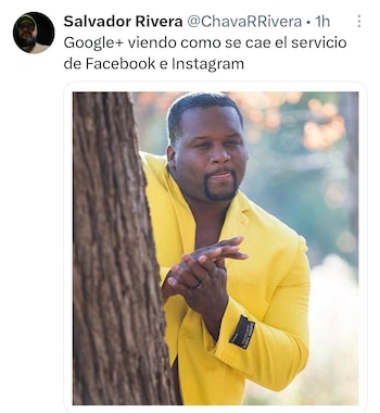 Un hombre de piel oscura con traje amarillo brillante y camisa abierta asoma por detrás de un tronco de árbol grueso, con una expresión traviesa y las manos juntas