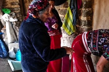 Tres mujeres con faldas rojas y prendas bordadas dentro de una habitación con paredes de piedra.