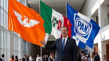 Vicente Fox Quesada, sonriendo y gesticulando con la mano derecha, de pie frente a tres banderas: naranja con ave blanca, mexicana con PRI, y azul con PAN.