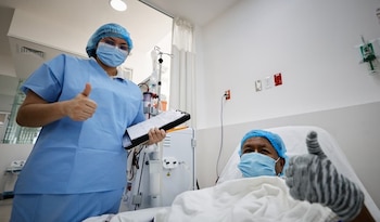 Una enfermera con uniforme azul y un paciente en cama de hospital, ambos con cubrebocas, dan pulgares arriba en una sala médica