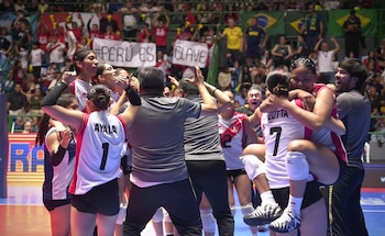 Jugadoras de voleibol con uniforme blanco y rojo abrazan a sus entrenadores en la cancha frente a la tribuna con espectadores