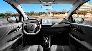 Vista del interior de un automóvil con volante, pantalla digital en el panel central, palanca de cambios y parabrisas