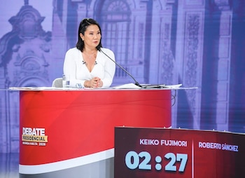 Keiko Fujimori sentada en un podio rojo y gris, con blusa blanca, manos entrelazadas y micrófono. Un cronómetro digital muestra su nombre