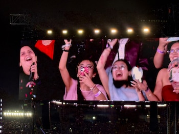 Una pantalla gigante proyecta a varios espectadores sonrientes que sostienen teléfonos móviles en un concierto nocturno