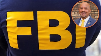 Espalda de persona con camiseta azul oscura que lleva el logo amarillo del FBI, y en un círculo, un hombre calvo sonriente con traje azul y corbata amarilla.