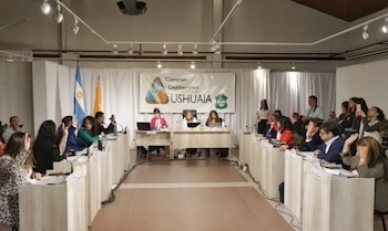 Integrantes de un cuerpo legislativo sentados ante escritorios levantan la mano frente a un cartel del Concejo Deliberante de Ushuaia