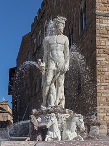 Estatua de mármol blanco de Neptuno de pie sobre un carro tirado por caballos marinos, con agua brotando a su alrededor, frente a un edificio antiguo de piedra