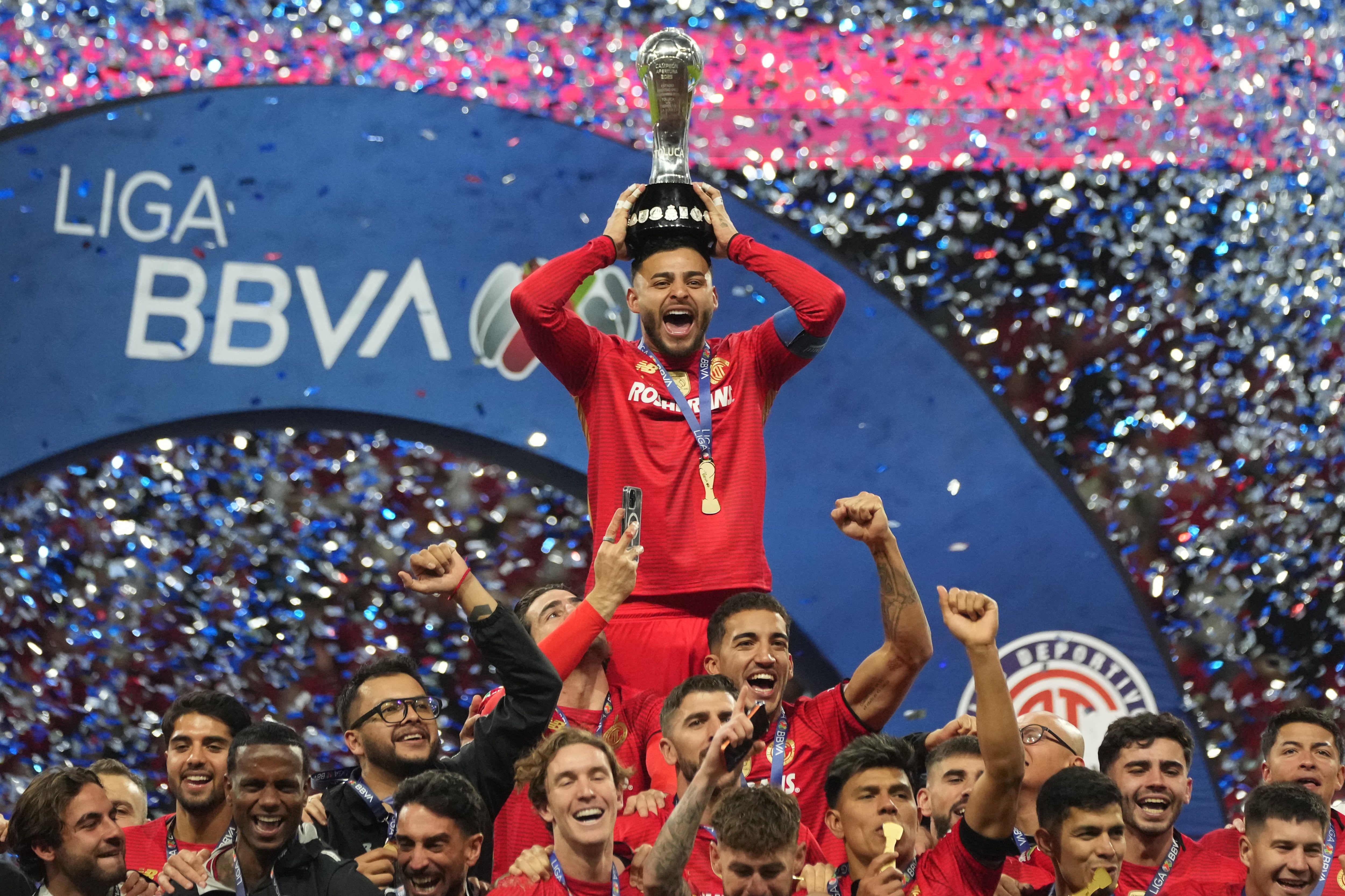 Alexis Vega, arriba, de los Diablos Rojos del Toluca, alza el trofeo después de que el equipo se coronara campeón de la Liga MX en tanda de penaltis frente a los Tigres, el domingo 14 de diciembre de 2025, en Toluca, México. (AP Foto/Eduardo Verdugo)