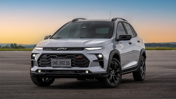 Primer plano frontal de un Chevrolet Sonic B-SUV gris claro con techo y detalles negros, estacionado en asfalto con un cielo de atardecer y horizonte verde de fondo