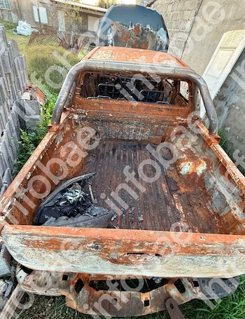 Vista trasera de la caja de una camioneta quemada, con la carrocería oxidada y restos calcinados en su interior, junto a un muro de concreto