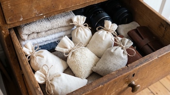 Un cajón de madera abierto revela varias bolsas de tela blancas y de arpillera, una de ellas con arroz visible, junto a toallas dobladas y lentes de cámara.