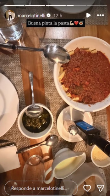Vista aérea de un plato de pasta rigatoni con salsa boloñesa, un tazón de pesto, pan, queso rallado y una jarra de leche en una mesa de madera