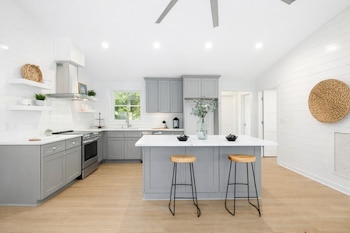 Cocina luminosa con isla central, taburetes de madera, gabinetes grises y pared decorada con cestas