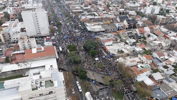 Vista aérea de una multitud masiva de personas ocupando una avenida urbana. Se observan edificios, árboles y vallas de seguridad a lo largo de la calle