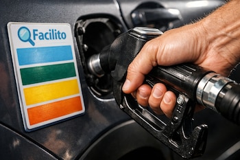Vista cercana de una mano sujetando una manguera de combustible insertada en el tanque de un automóvil gris oscuro, con una tarjeta "Facilito" y franjas de colores adyacente.