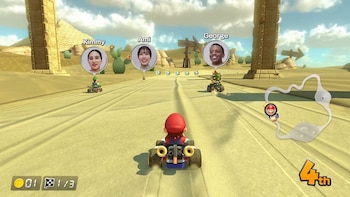 Mario en un kart sobre una pista de arena en el desierto con pirámides al fondo y otros corredores con fotos de perfil encima
