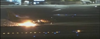 Un avión en una pista nocturna de aeropuerto emite una ráfaga de chispas y fuego en la parte inferior de su estructura
