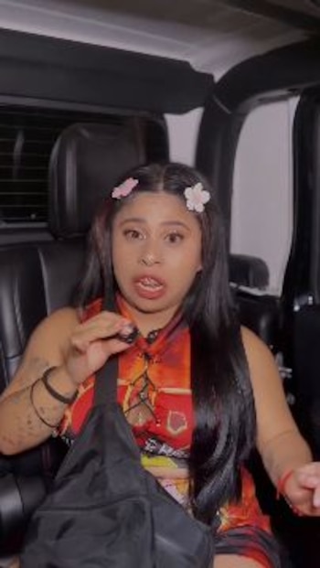 Una mujer con cabello largo y broches de flores en el cabello está sentada en el interior de un automóvil