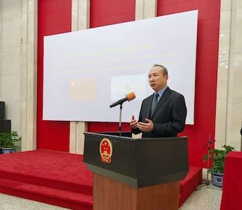 Embajador Wang Wei, vestido de traje, habla desde un podio con el emblema de China. Detrás, una pantalla exhibe las banderas de China y Argentina y texto de bienvenida